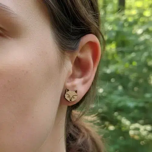 Boucle d'oreille en bois gravée tête de renard portée à l'oreille d'un enfant et nature verte flou e en arrière-plan